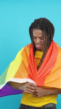 Lgbt bayrağıyla sarılmış mavi arka planlı mutlu Latin adam.