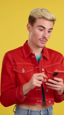 Stüdyoda sarı arka planı olan bir cep telefonunun ekranına bakan eşcinsel bir adam.