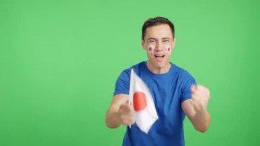 Stüdyoda, Japonya 'yı coşkuyla alkışlayan ve ulusal bayrak sallayan bir adamın krom görüntüsü var.