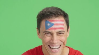 Stüdyoda, yüzünde Porto Riko bayrağı olan ve kameraya gülümseyen bir adamın krom görüntüsü var.