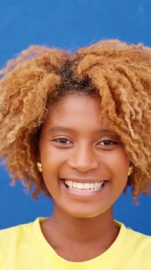 Mavi duvarın yanında kameraya gülümseyen Afrikalı bir kadının yavaş çekim videosu.