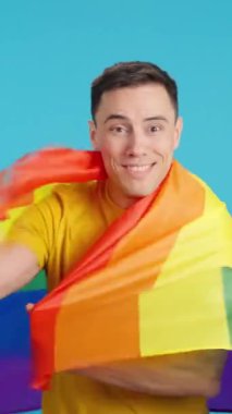 Lgbt gökkuşağı bayrağıyla sarılan mutlu bir adamın mavi arkaplanlı videosu stüdyoda. Çerçeve boş başlar, adam aşağıdan görünür ve altta kaybolur.