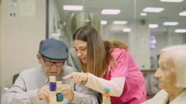 Dost canlısı bir hemşirenin yaşlı bir adama yetenek oyununda yardım ettiği ve sonra gülümsediği bir video.