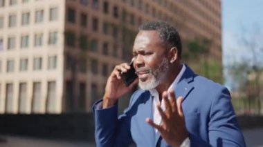 Dışarıda cep telefonuyla konuşurken koşan endişeli bir Afrikalı işadamının videosu.