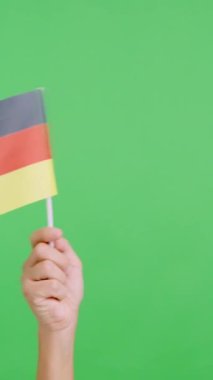 Stüdyoda, bir elin krom renginde, Almanya bayrağının bayrağını sağa sola salladığı yavaş çekim videosu.