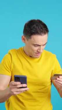 Stüdyoda cep telefonu ve kredi kartıyla alışveriş yapan mutlu bir adamın mavi arka planlı videosu var. Çerçeve boş başlar, adam aşağıdan görünür ve altta kaybolur..