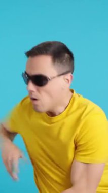 Stüdyoda, uyuşturucu almış, güneş gözlüklü, kontrolsüz dans eden bir adamın mavi arka planlı videosu kendini kaybediyor.