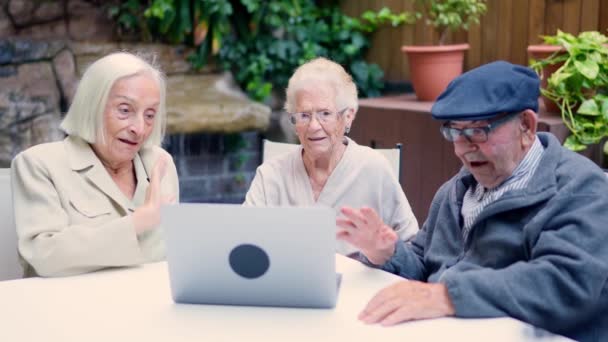 Видео Три Пожилых Человека Машут Время Видеозвонка Ноутбуком Сидящим Саду — стоковое видео