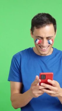 Yüzünde Fransa bayrağı olan ve cep telefonuna bakıp gülümseyen ve krom tuşlu ekranla kameraya gösteren Fransız bir adamın krom arka planına sahip bir video..
