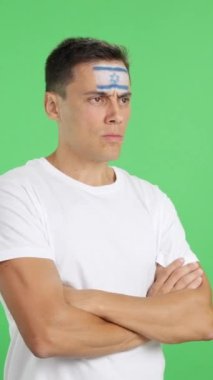 Stüdyoda, yüzünde İsrail bayrağı olan bir adamın ciddi bir ifadeyle yüzünü boyadığı bir video.