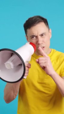 Stüdyoda, izleyicilere megafonla konuşan bir liderin mavi arkaplanlı videosu var.