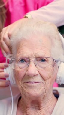 Yaşlı bir kadına kulaklık takan bir hemşirenin videosu.