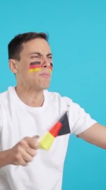 Stüdyoda, elinde Alman ulusal bayrağı sallayan, hakemlerin kararına kızgın bir adamın krom görüntüsü var.