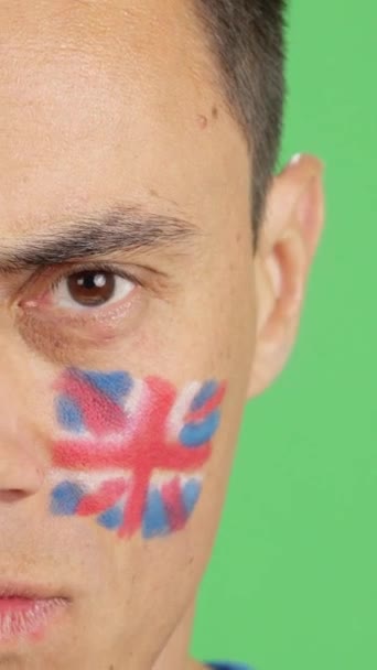 カメラを見ている顔にイギリスの国旗を塗った深刻な男のクロマのスタジオでのビデオ — ストック動画