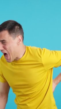 Stüdyoda mavi arka planı olan bir adam, sırt ağrısı çektiğini söylüyor.