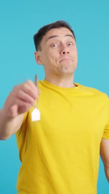 Yeni alınmış bir evin anahtarlarını gösteren mutlu bir adamın mavi arkaplanlı videosu stüdyoda.