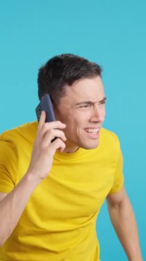 Cep telefonundan duyduklarını dinlemeye çalışan bir adamın mavi arka planlı videosu stüdyoda.