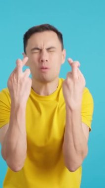 Stüdyoda mavi arka planı olan bir adam şans diliyor.