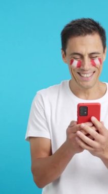 Yüzünde Peru bayrağı olan Perulu bir destekçinin krom arkaplanlı stüdyo videosu, cep telefonuna bakıp gülümsüyor ve krom tuşlu ekranla kameraya gösteriyor.