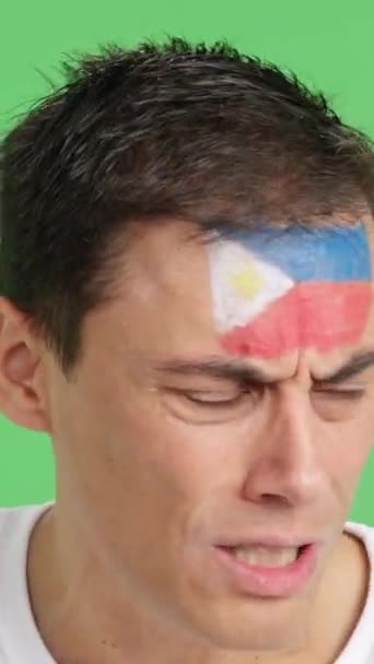 在演播室里用彩色照片近距离拍摄一个脸上涂有菲律宾国旗的非常紧张的男人的照片 在一场最后以失败告终的艰难的比赛中支持菲律宾队 — 图库视频影像