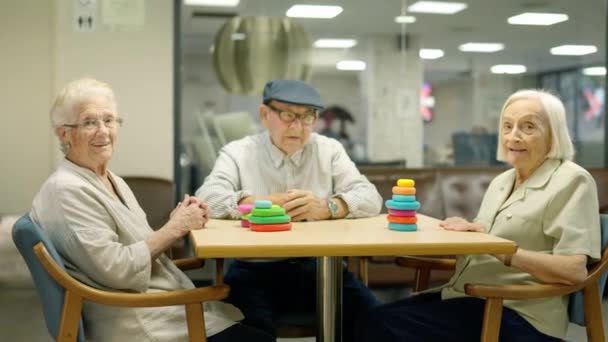 三个老年人坐在一张桌子旁边看着相机的视频 桌子上有一个疗养院的游戏 — 图库视频影像