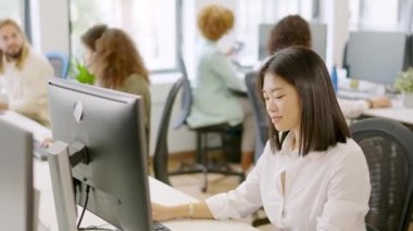 Asyalı bir kadının diğer iş arkadaşlarıyla birlikte çalışma alanında mutlu bir şekilde çalışmasının yavaş çekim videosu.