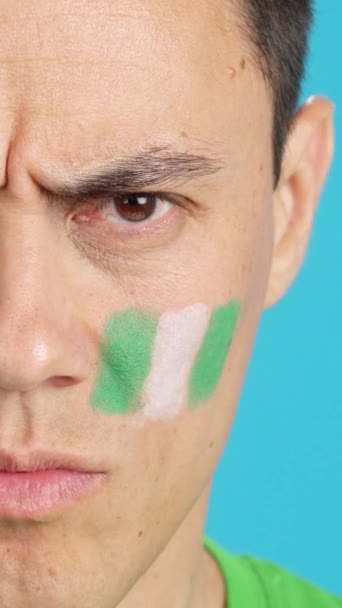 カメラを見ている顔にナイジェリアの旗を塗った深刻な男のクロマのスタジオでのビデオ — ストック動画