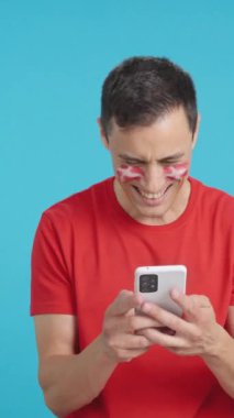 Danimarkalı bir destekçinin krom arkaplanlı stüdyo videosu. Yüzünde Danimarka bayrağı var. Cep telefonuna bakıp gülümsüyor ve ekranda kroma tuşuyla onu gösteriyor.