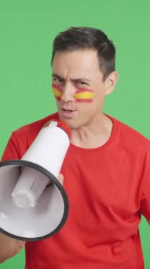 Stüdyoda, yüzünde İspanyol bayrağı olan bir adamın megafonla kalabalığı topladığı bir video.