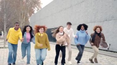 Sokakta birlikte koşan çok ırklı, oyuncu ve mutlu bir grup arkadaşın yavaş çekim videosu.
