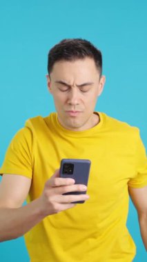 Stüdyoda üzgün bir adamın suratında hoşnutsuz bir ifadeyle cep telefonuna baktığı mavi arka planlı bir video var. Çerçeve boş başlar, adam aşağıdan görünür.