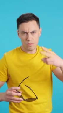 Stüdyoda, güneş gözlüğünü takmaya çalışan bir pezevengin mavi arka planlı videosu.