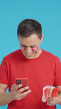 Yüzünde Kanada bayrağı olan Kanadalı bir destekçinin krom arka planına sahip bir stüdyo videosu, cep telefonuna bakıp gülümsüyor ve ekranda kroma tuşuyla onu gösteriyor.