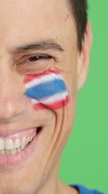 Stüdyoda, yüzünde Tayland bayrağı olan ve kameraya gülümseyen bir adamın krom görüntüsü var.