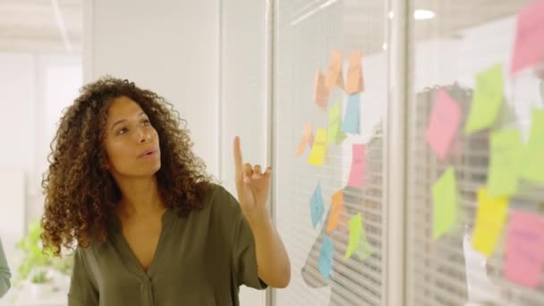 粘着ノートを使用した女性のスローモーションビデオと 同僚でアイデアを提示するためにそれらのいずれかを指す — ストック動画