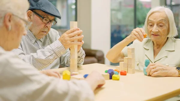 stock image Three concentrated seniors resolving brain skill games with wooden pieces in a geriatric