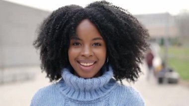 Kamerayla yavaş çekim videosu dışarıda kameraya gülümseyen Afrikalı genç bir kadına yaklaşıyor.