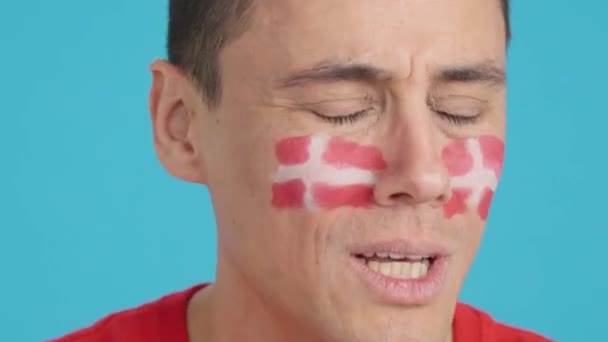 在演播室里用彩色的特写拍摄了一个非常紧张的男人 他的脸上挂着一面丹麦国旗 在一场最后以失败告终的艰难的比赛中 他支持着一支丹麦球队 — 图库视频影像