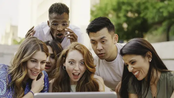 Multiethnic group of people looking at a laptop screen with surprised expression in the street