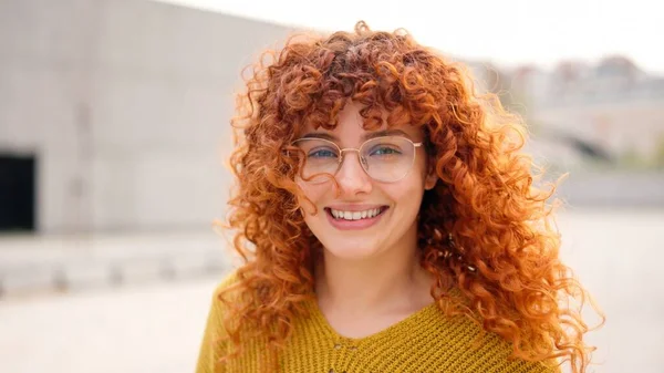 Young and redhead woman with curly long hair smiling at camera