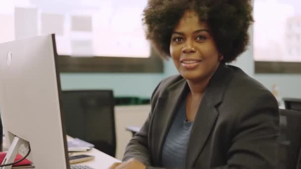 一位非洲裔美国女同事坐在办公室里对着摄像机笑的水平慢镜头 — 图库视频影像