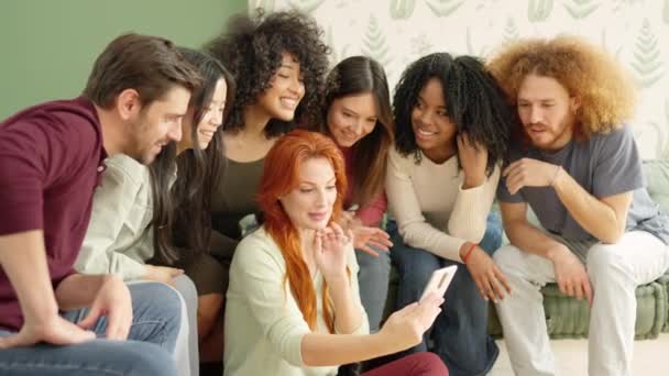 多种族朋友看着一个女人的手机 坐在沙发上笑着看其中一个视频的慢镜头 — 图库视频影像