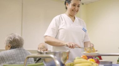 Yaşlı insanlara yemek servisi yapan gülümseyen bir kadının yavaş çekim videosu.