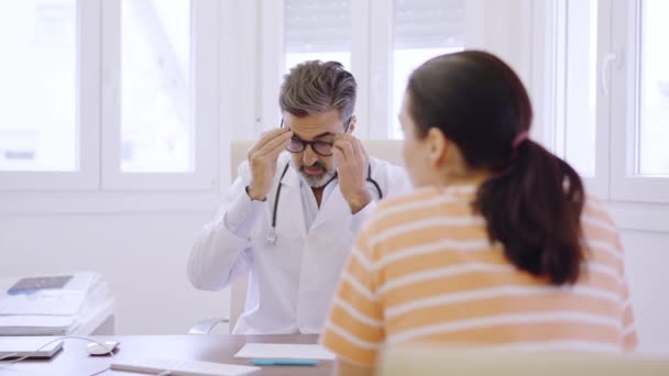 眼鏡を調整し ノートを書き クリニックに座っている女性患者と話す成熟した医師のスローモーションビデオ — ストック動画