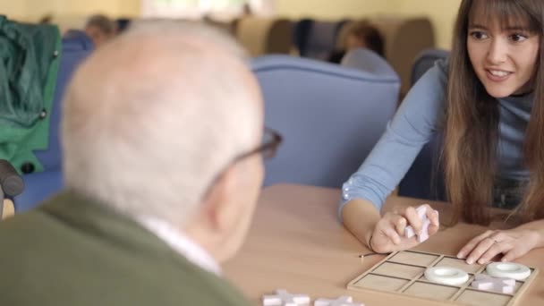 一个女孩在养老院向一位老人解释游戏规则的慢镜头 — 图库视频影像