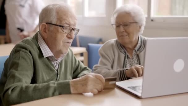老年妇女用笔记本电脑和信用卡向男人解释如何上网购物的慢镜头 — 图库视频影像