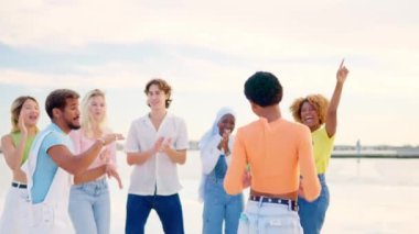 Gün batımında deniz kenarında dans eden çok ırklı arkadaşlara yaklaşan yavaş çekim videosu