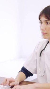 Klinikteki bir masada bilgisayarını kullanan konsantre bir kadın doktorun yavaş çekim videosu.