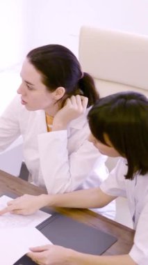 Klinikte bilgisayar kullanarak tıbbi raporları tartışan iki kadın doktorun yavaş çekim videosu.