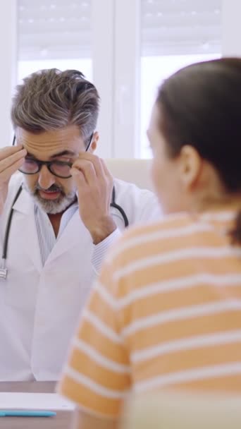 一个成熟医生调整眼镜 写下笔记和与坐在诊所里的女病人交谈的慢动作视频 — 图库视频影像